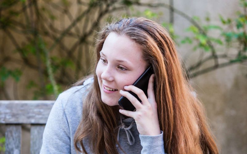 Rødhåret pige sidder på en bænk og taler i telefon