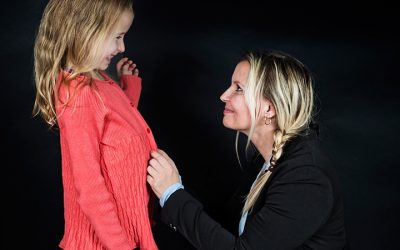 Kvinde på hug kigger på pige i rød sweater