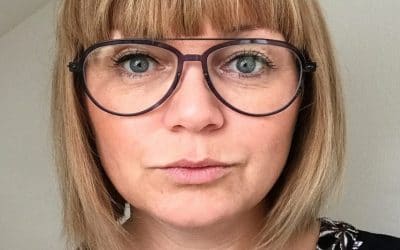 Blond kvinde med briller kigger ind i kameraet