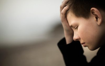 Dreng med mørkt hår kigger ned med hånden i panden