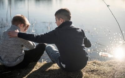 En dreng trøster en anden dreng ved en sø