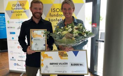 To voksne står og holder fundraisingprisen og en buket blomster