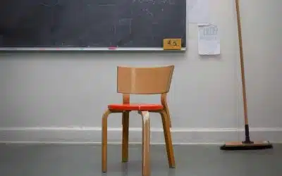En stol af tre med rødt sæde står i hjørnet af et klasselokale, med en kost og en tavle i baggrunden.