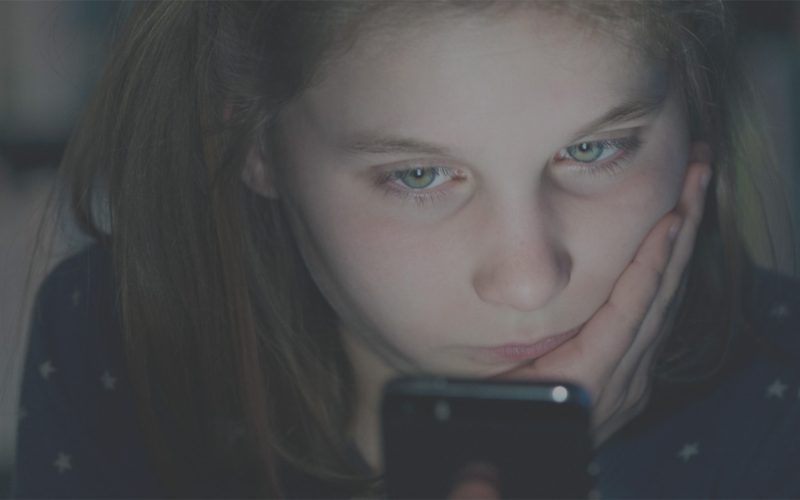 Brunhåret pige med grønne øjne kigger ind på en telefon.