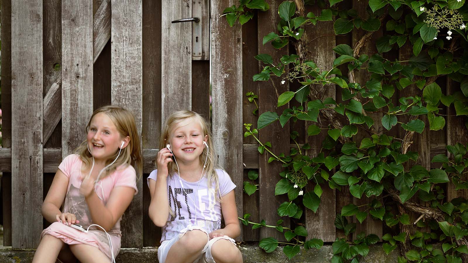 To piger sidder foran et hegn med høretelefoner i