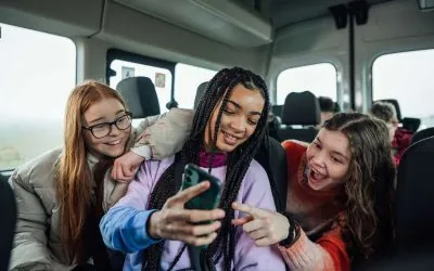 Tre piger sidder i en bus og kigger på en mobil