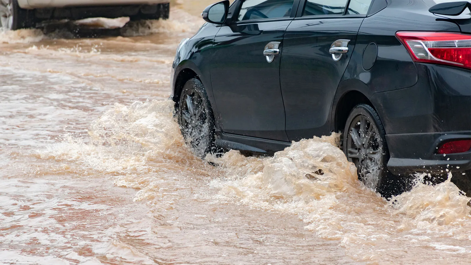 Sort bil kører igennem oversvømmet vej