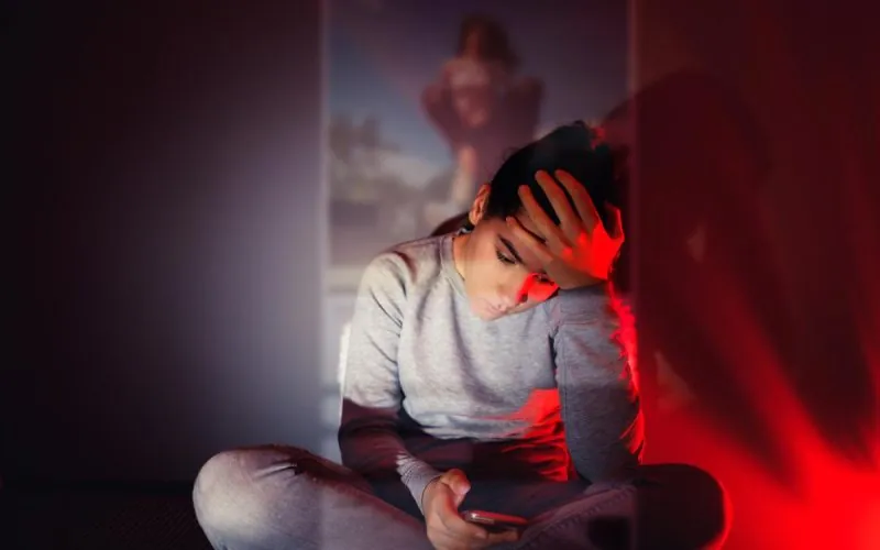 Dreng sidder i rødt lys og kigger på sin telefon