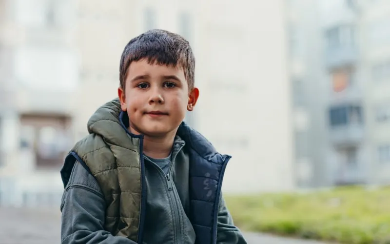 Mørkhåret dreng foran nogle slørrede bygninger kigger ind i kameraet