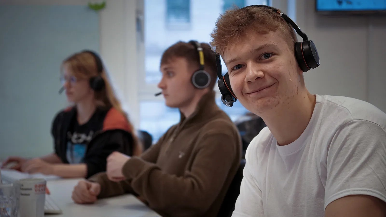 En mand sidder med headset på med to slørede mennesker med headset på i baggrunden